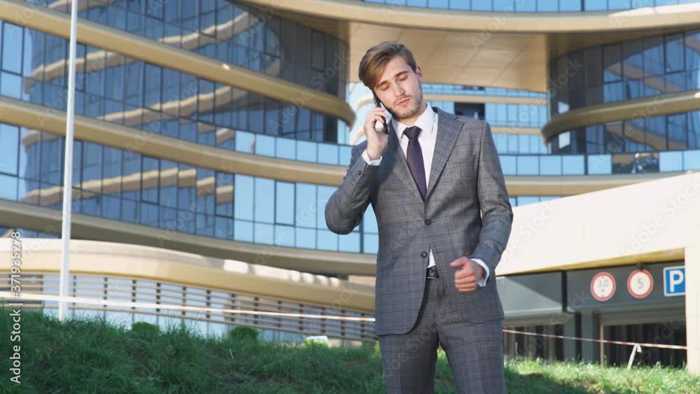 Businessman, top manager in a suit stands near a glass skyscraper and talking on a mobile phone, young businessman manager near the office. Businessman, top manager in a suit stands near a glass skyscraper and talking on a mobile phone, young businessman manager near the office.