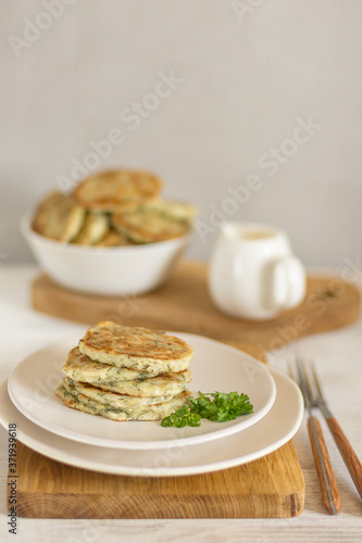 Zucchini pancakes with herbs on a light plate and a wooden board