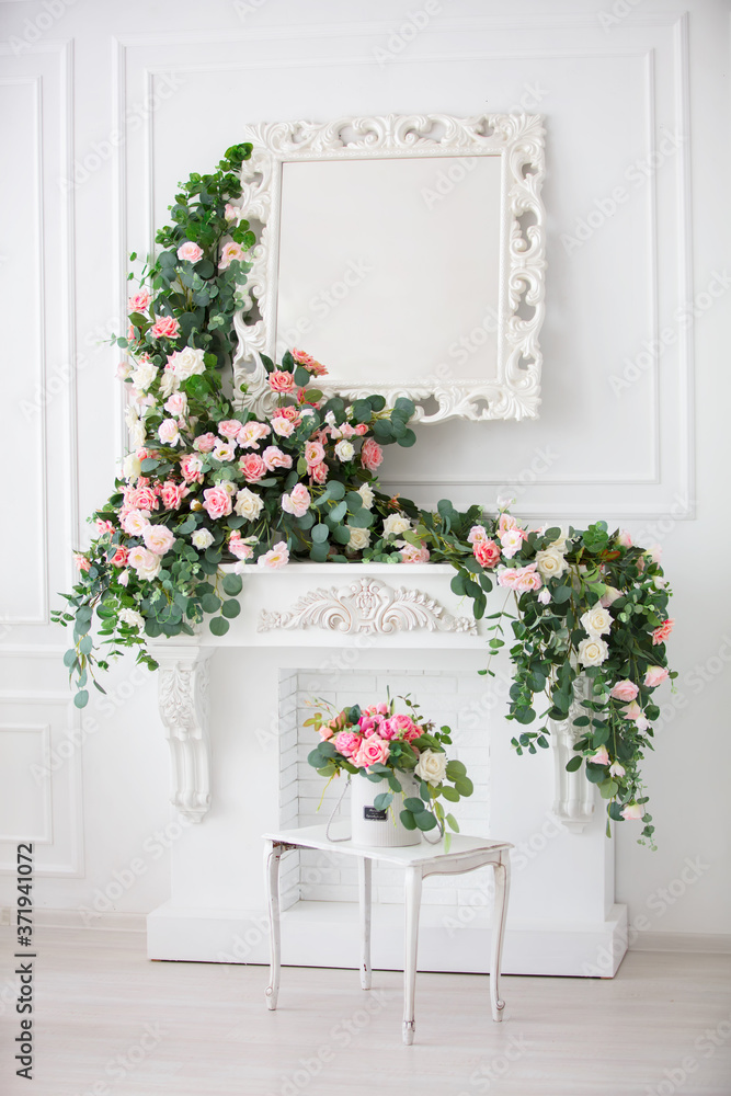 Vertically, the interior of a white room decorated with pink flowers. White fireplace, mirror and flower garlands. Vertically, the interior of a white room decorated with pink flowers. White fireplace, mirror and flower garlands.