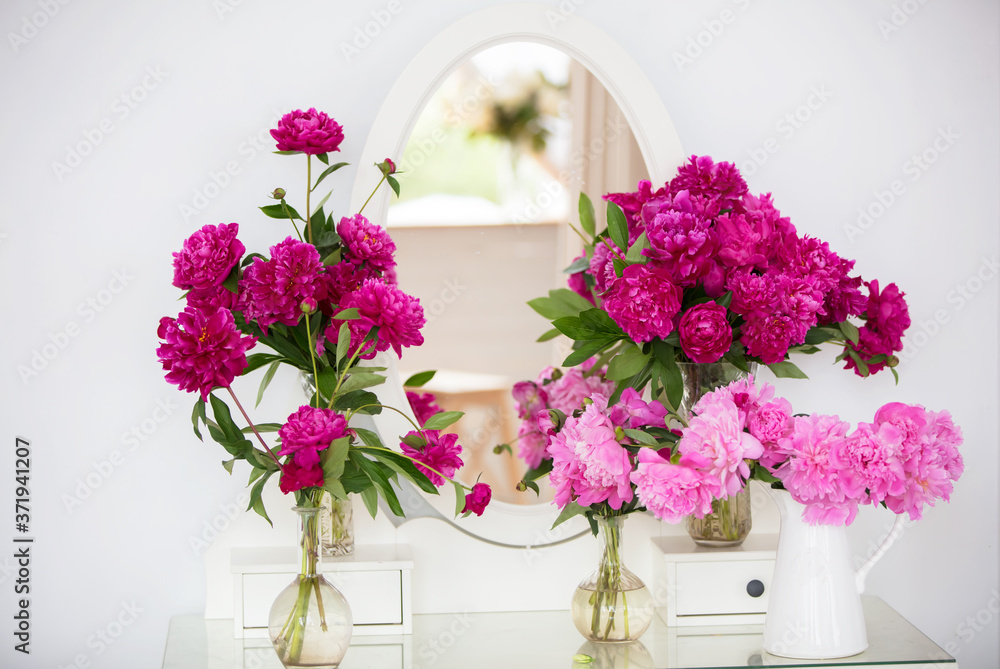 Bright peonies against a white wall and a mirror.
