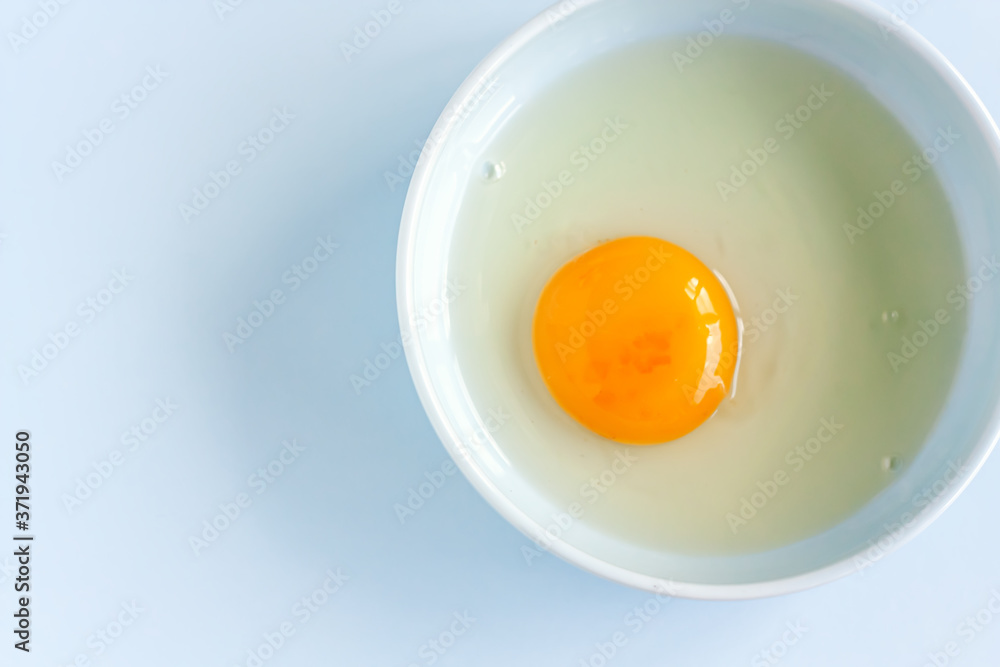 Fresh organic raw yolk and white of egg in light blue bowl on pastel background. Healthy breakfast and fresh ingredients. Selective focus. Top view. Space for text. Fresh organic raw yolk and white of egg in light blue bowl on pastel background. Healthy breakfast and fresh ingredients. Selective focus. Top view. Space for text.