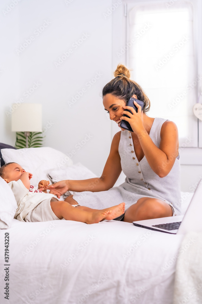 Young Caucasian mother with her son in the room on top of the bed. Mother teleworking and caring for her child, a new normal after the coronavirus pandemic, covid-19. Social distance