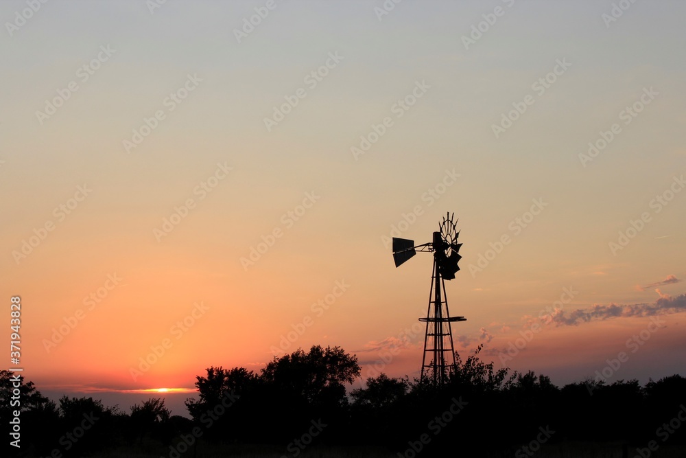 Kansas colorful Sunset with sky and clouds with a Windmill silhouette out in the country north of Hutchinson Kansas USA.