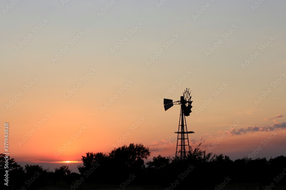 Fototapeta premium Kansas colorful Sunset with sky and clouds with a Windmill silhouette out in the country north of Hutchinson Kansas USA.