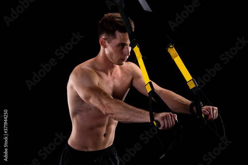 Young muscular man exercising with fitness straps isolated on black background. Active lifestyle. Total resistance exercises