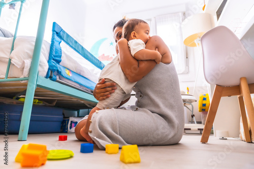 Young Caucasian mother playing with her in the room with toys. Baby less than a year learning the first lessons of her mother. Mother playing with her son and hugging him lovingly