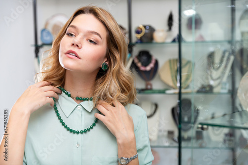 Stylish young female client choosing natural gemstone jewelry in boutique, trying on beads of polished green nephrite photo