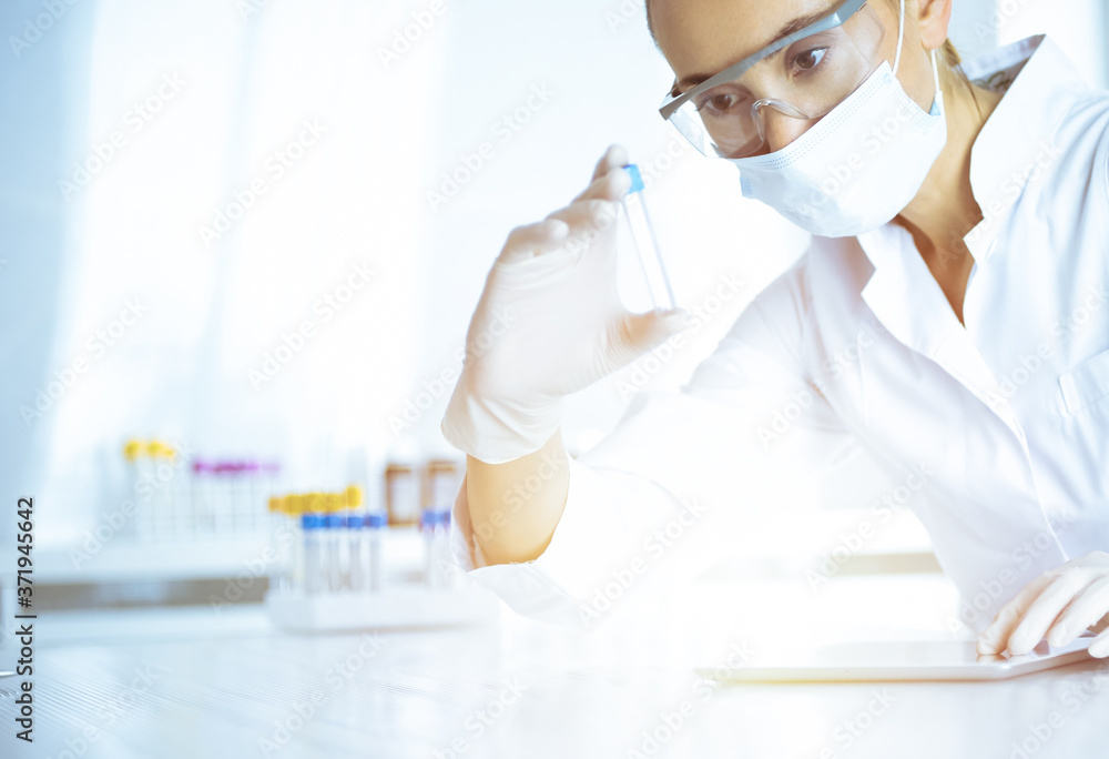 Female laboratory assistant analyzing a blood sample at hospital. Medicine, health care and researching concept
