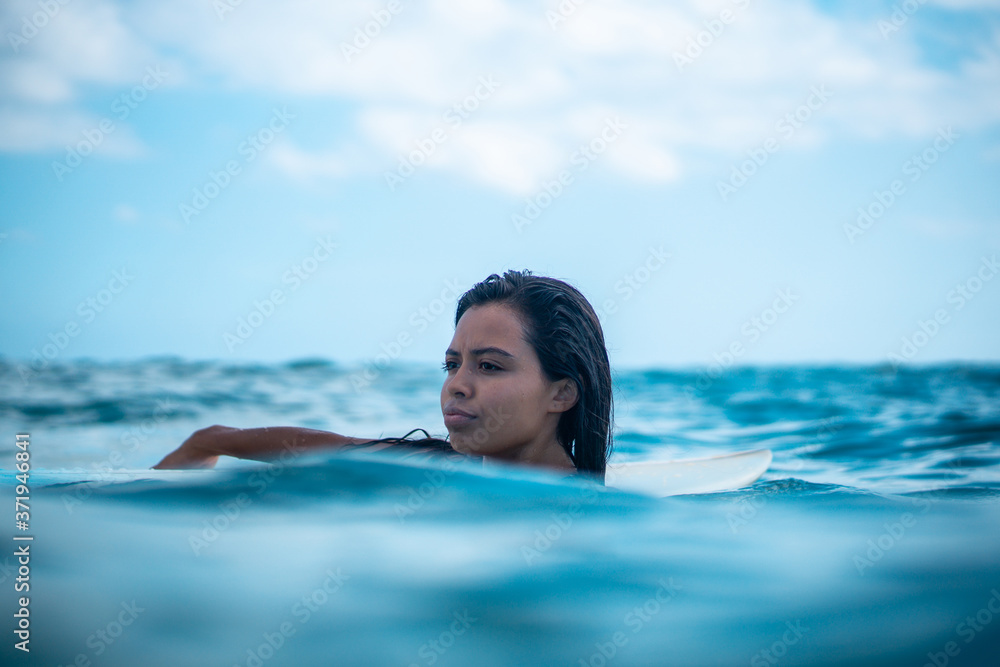 Portrait of surfer girl on white surf board in blue ocean pictured from the water in Bali