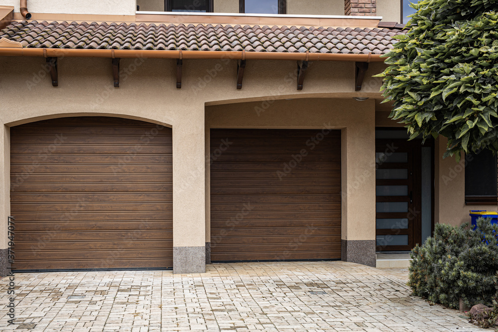 Brick stone driveway double garage doors with green tree. Elegant brown house driveway
Brick stone driveway double garage doors with green tree. Elegant brown house driveway