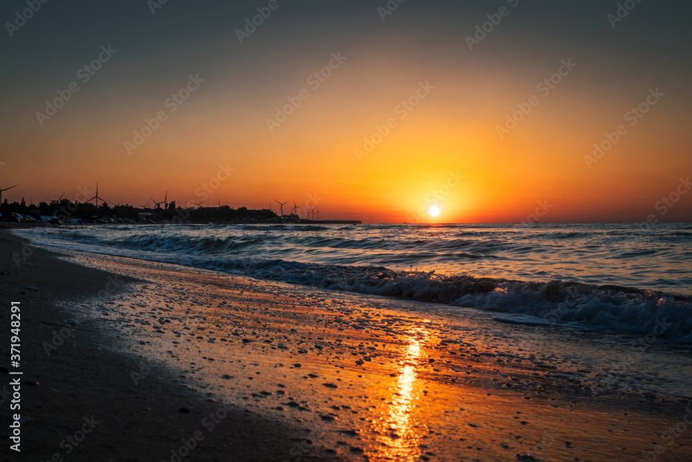 sunrise at sea with waves and windmills on background