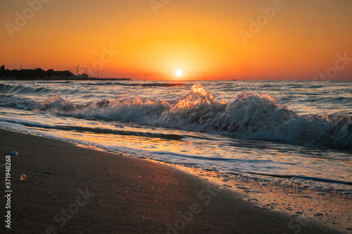sunrise at sea with waves and windmills on background