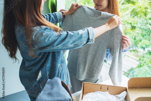 Two young women receiving a postal parcel box and try on clothes at home for delivery and online shopping concept photo