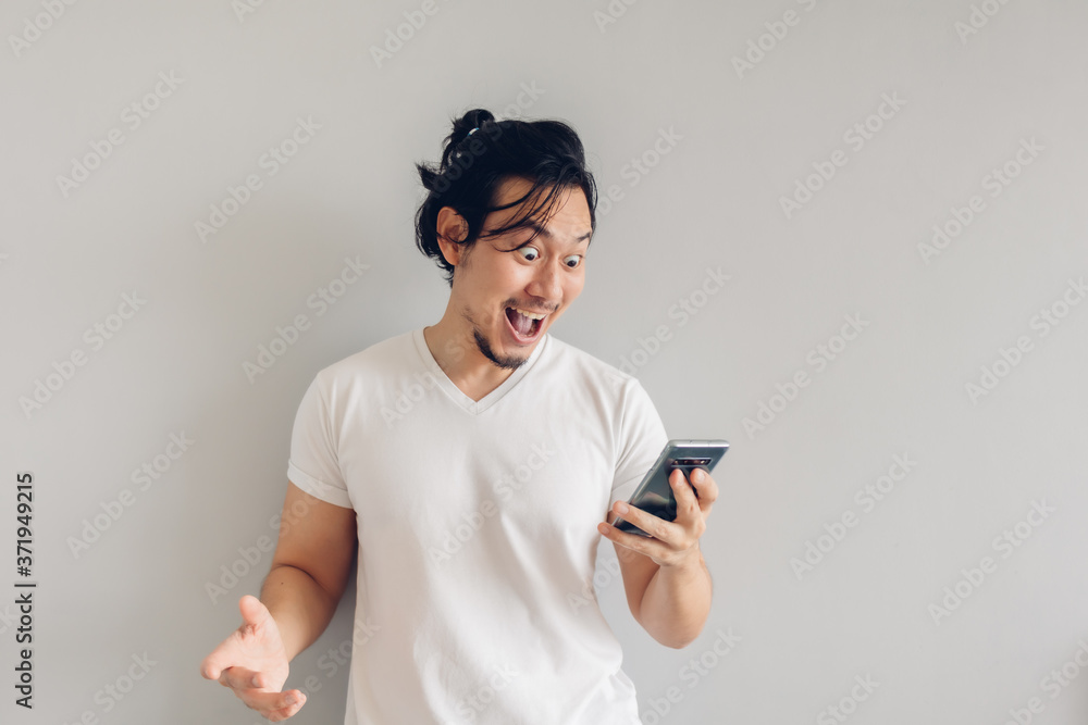 Surprised and shocked long hair Asian man in white t-shirt is using smartphone. Surprised and shocked long hair Asian man in white t-shirt is using smartphone.