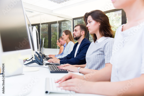 Side view of row of ordinary business people working with computers in modern open plan office