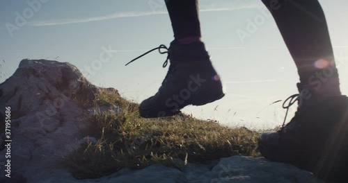 Active young woman climb on top peak of rock or cliff for a view in hiking or mountaineering boots or shoes footwear on an autumn or fall hike unrecognizable slowmotion with morning sunrise flare