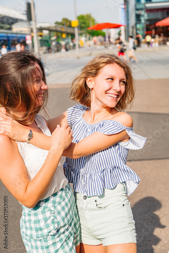 Two young girls friends walk in city in summer day