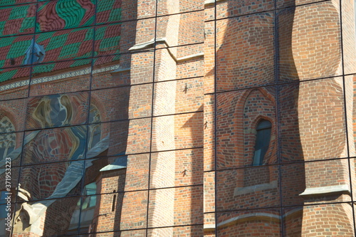 Reflection of an old, gothic church with a multi-colored roof and beautiful architectural forms in the glass of a new modern building against a blue sky, wallpaper for the screen