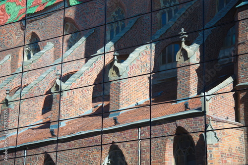 Reflection of an old, gothic church with a multi-colored roof and beautiful architectural forms in the glass of a new modern building against a blue sky, wallpaper for the screen