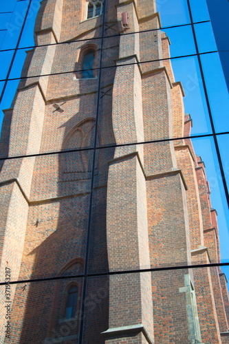 Reflection of an old, gothic church in the glass of a new s, a modern building against a blue sky in a horizontal position, a screensaver for a mobile phone