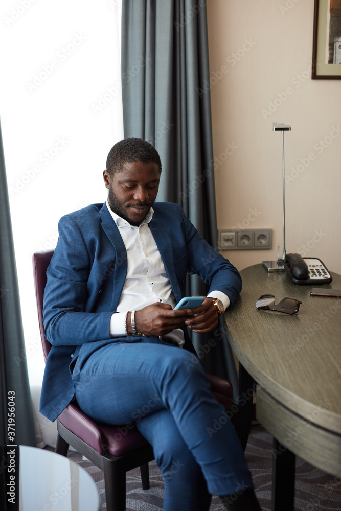 young african businessman sitting on chair in hotel, using smartphone, chat with business partner, have rest