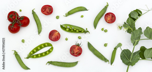 Red cherry tomatoes and green peas on white wooden table. Fresh summer vegetables for food concept, top view, flat lay, banner