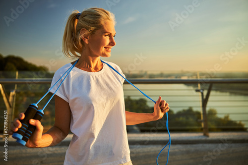 Cheerful woman with skipping rope standing on the street