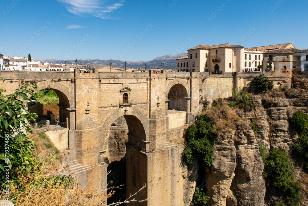 View of Ronda, Andalusian town situated atop spectacular deep gorge, with a massive stone bridge with arches, traditional Spanish buildings and blue sky, Spain.