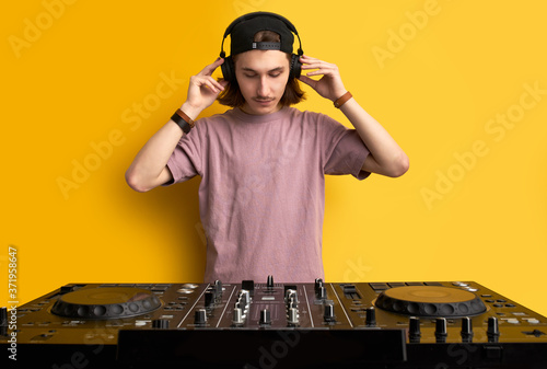 dj man in white headphones behind dj console, makes song with dj controller. long haired caucasian guy in cool stylish wear posing on isolated background