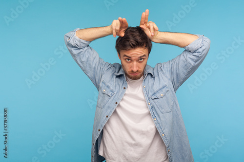 Canvas Print Portrait of aggressive man in worker denim shirt standing with bull horn gesture and looking menacingly at camera, threatening to attack, provoking conflict