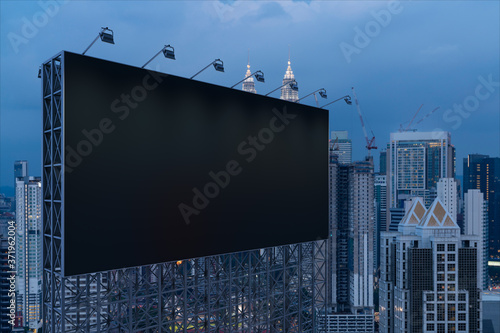 Blank black road billboard with KL cityscape background at night time. Street advertising poster, mock up, 3D rendering. Side view. The concept of marketing communication to promote or sell idea. photo