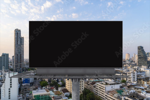 Blank black road billboard with Bangkok cityscape background at sunset. Street advertising poster  mock up  3D rendering. Front view. The concept of marketing communication to promote or sell idea.