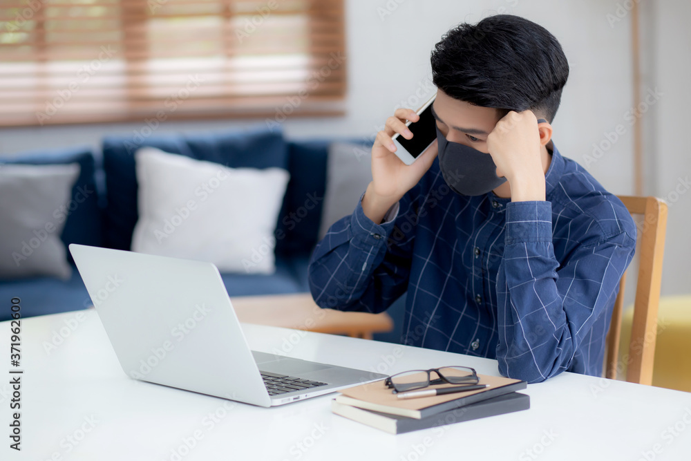 Young asian business man in face mask talking smartphone and work on laptop computer for protect covid-19, businessman quarantine work from home with notebook, social distancing and stay home. Young asian business man in face mask talking smartphone and work on laptop computer for protect covid-19, businessman quarantine work from home with notebook, social distancing and stay home.