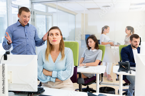 Upset girl sitting at laptop in coworking space while dissatisfied annoyed businessman pointing out mistakes in her work