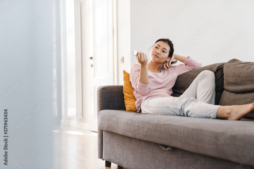 Smiling asian girl lying on the sofa watching tv Smiling asian girl lying on the sofa watching tv