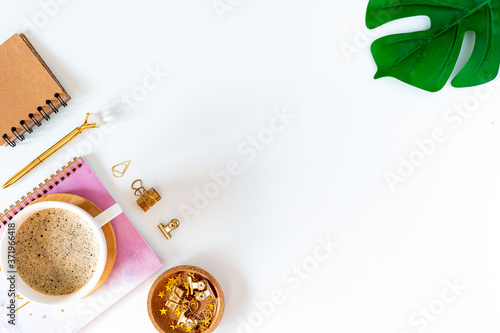 Flat lay of white working table place background with cup of coffee putting on it. Top view glasses, leaf, golden paper binder clips, Notebook and pen. Desktop mock up scene with copy space