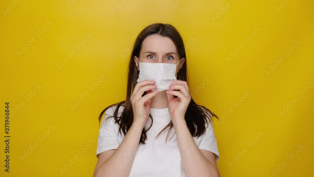 Young caucasian woman protects face with mask, thinks about risk of epidemic disease, has virus infection, isolated on yellow background. Concept health and safety, N1H1 coronavirus, virus protection Young caucasian woman protects face with mask, thinks about risk of epidemic disease, has virus infection, isolated on yellow background. Concept health and safety, N1H1 coronavirus, virus protection