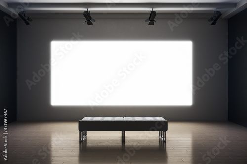 Modern exhibition room with blank projection screen and bench photo