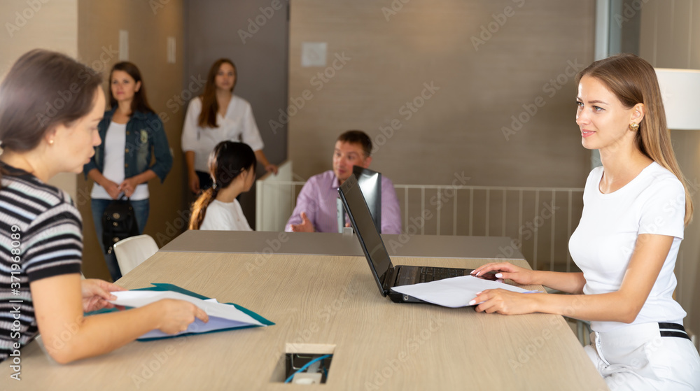 Smiling young woman assistant of notary public receiving customers in hall of modern office ..