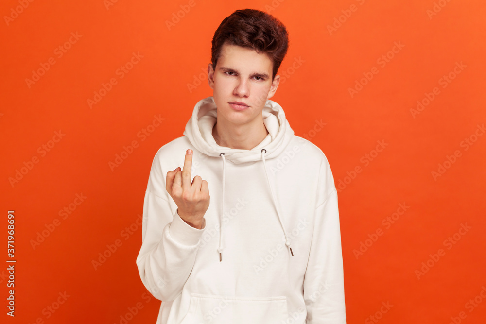Rude selfish teenager in casual white hoodie showing middle finger at camera, back off, aggression gesture. Indoor studio shot isolated on orange background Rude selfish teenager in casual white hoodie showing middle finger at camera, back off, aggression gesture. Indoor studio shot isolated on orange background