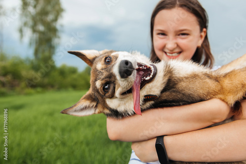 Smiling teenage girl holding a happy dog ​​in her arms, looking at the camera #371968896