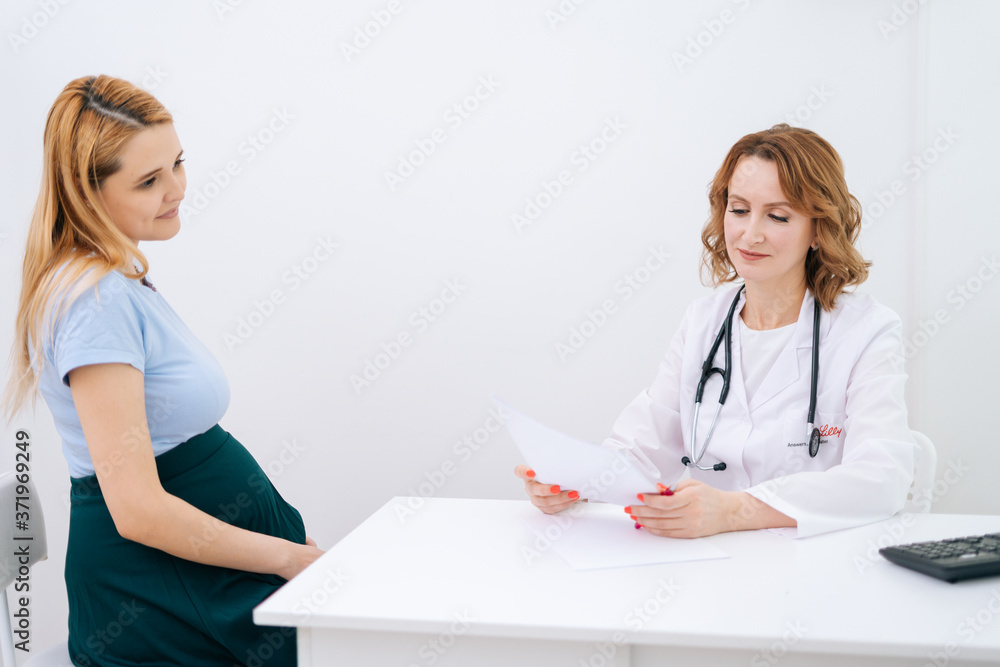 Attractive young pregnant woman with blonde hair came to doctor with folder of paper documents. Doctor examine pregnant belly for baby and mother healthcare check up. Attractive young pregnant woman with blonde hair came to doctor with folder of paper documents. Doctor examine pregnant belly for baby and mother healthcare check up.