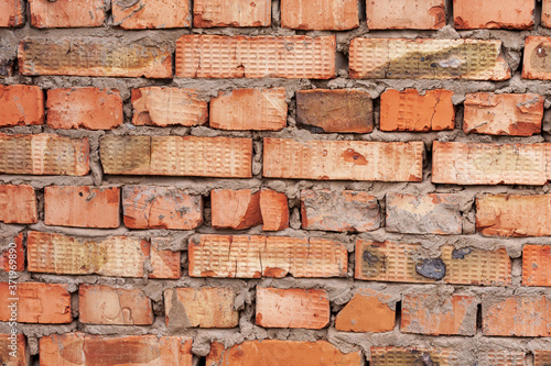 The wall is made of old non-uniform red brick of different shades, fastened with cement mortar, as the base of the house. Individual bricks with chips, with various notches and notches.