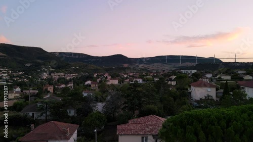 Evening golden hour aerial view o small historic town of Millau, France. Drone overflying scenic french city flying toward Millau viaduct nested between the hills.
