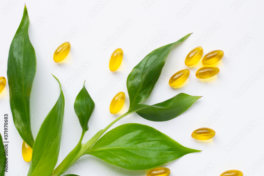 Capsules with fish oil and vitamins A and E, green leaves. Health care