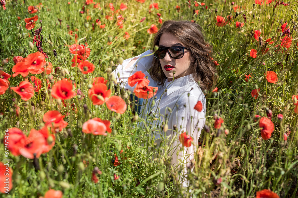 Young woman is standing near blooming poppy field Young woman is standing near blooming poppy field