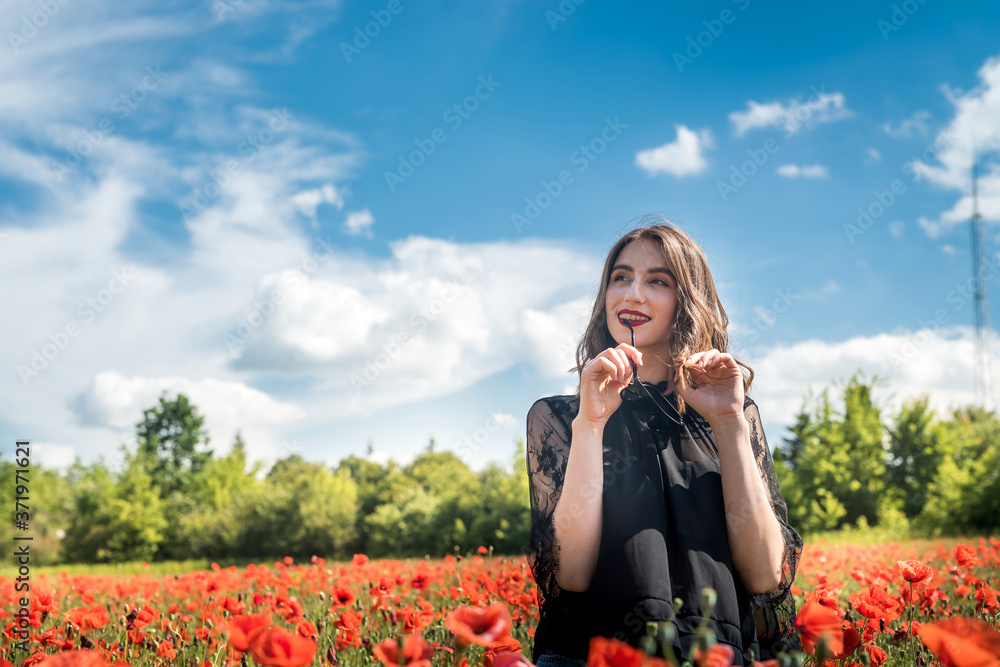 Young woman is standing near blooming poppy field