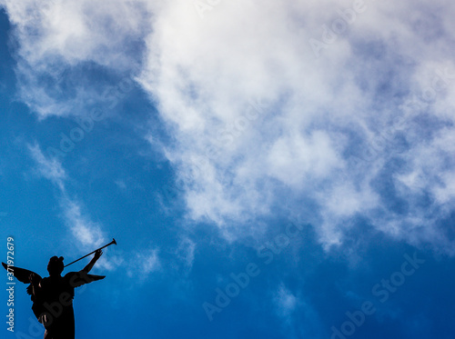 Angel and clouds in the sky. Angel looking at the sky and blowing a trumpet against the clouds