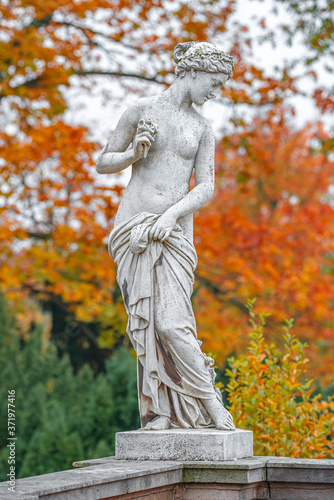 Old park statue of sensual half naked Greek or Italian Renaissance Era woman with flowers in city park went to golden Autumn, Potsdam, Germany