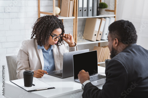 Millennial African American businesswoman having conflict with collague at workplace, empty space photo